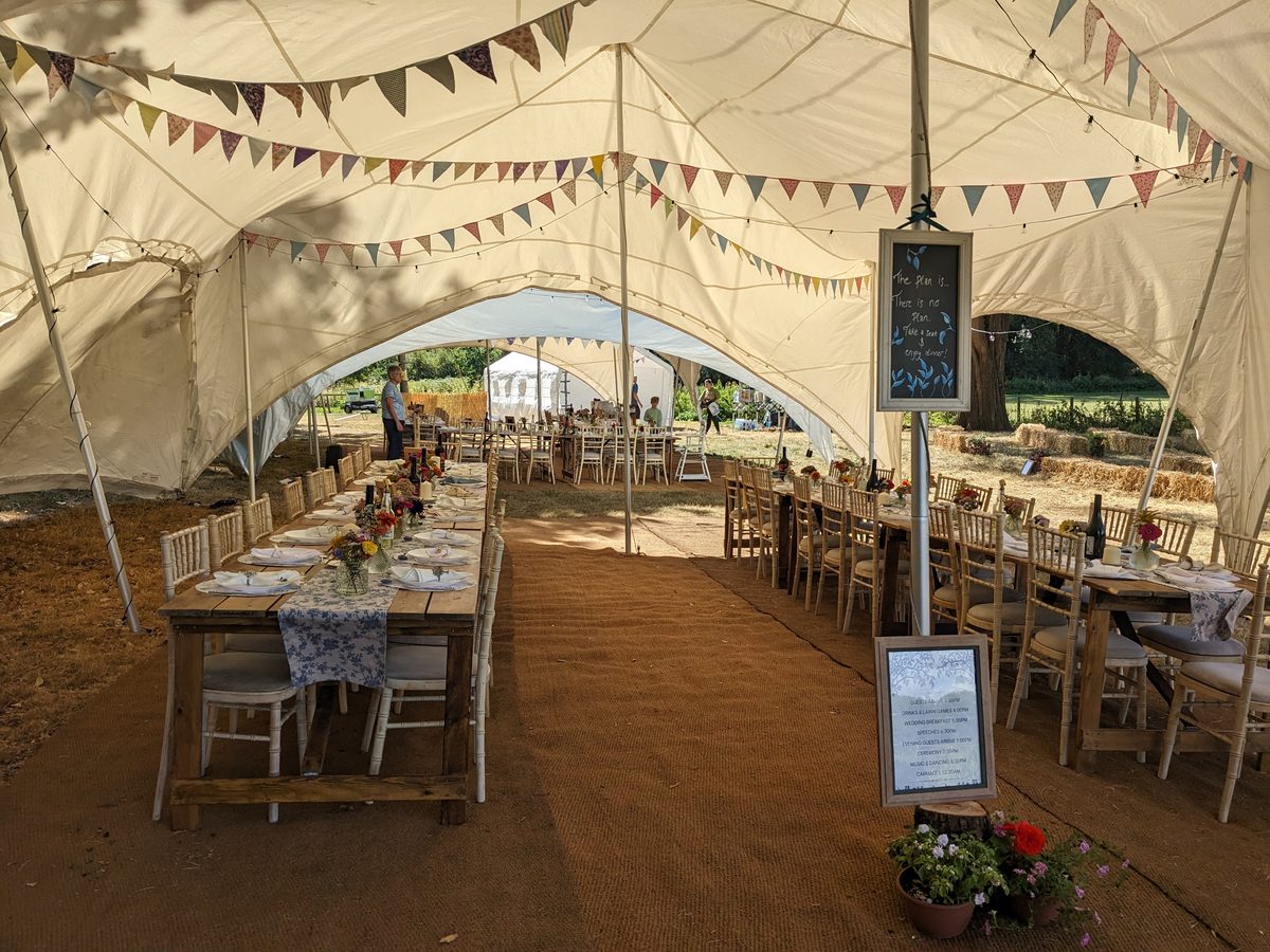 Long tables laid for a wedding feast under a marquee hung with bunting